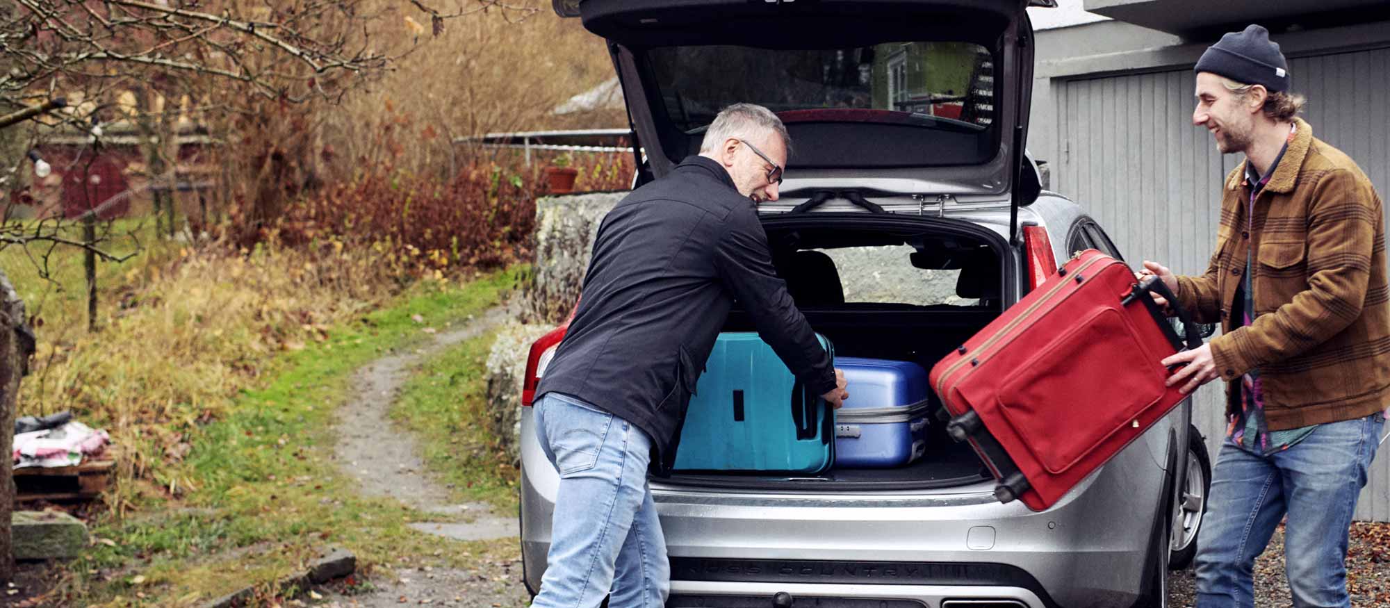 Två män packar in resväskor i bagageluckan på en bil